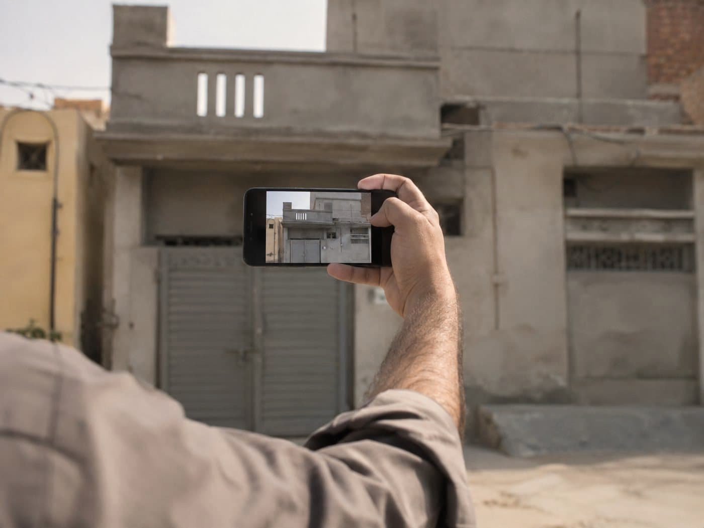 A man holding up a phone to photograph the front of a house